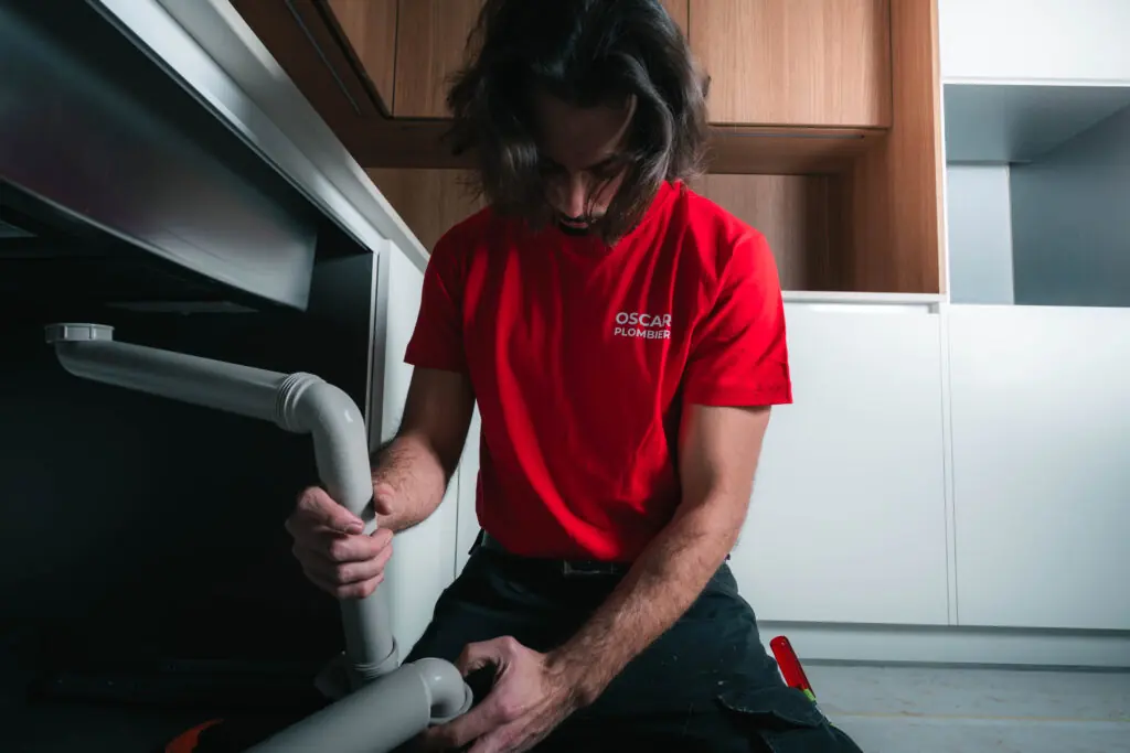 Technicien Oscar Plombier posant une installation sanitaire sous un évier